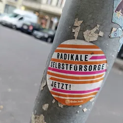 A round sticker with orange and pink stripes. The text on the sticker says "Radikal Selbstfürsorge Jetzt!" which translates to "Radical Self-Care Now!" in German.  There is also an Instagram handle on the bottom of the sticker.