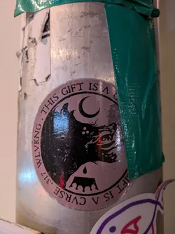 Round sticker with a dark, illustrated wolf, moon, and crown. Text reads: "THIS GIFT IS A CURSE. WLKVNG."