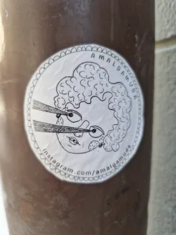 This round sticker showcases a hand-drawn illustration of a person with curly hair, expressive eyes, and what appears to be a ray of light or a whisker emerging from their face. The style is whimsical and slightly surreal. The artist's Instagram handle is printed at the bottom of the sticker.