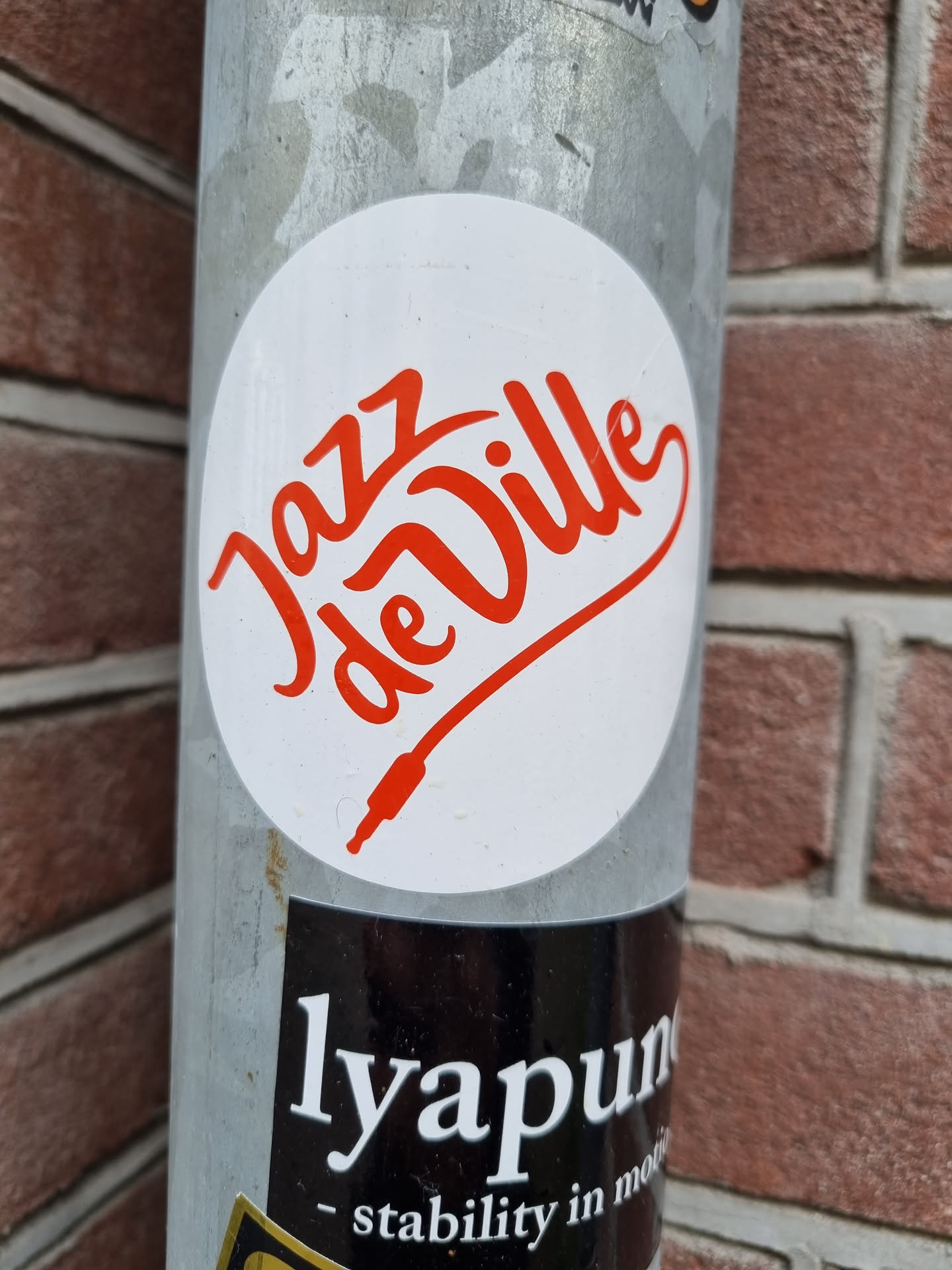Round white sticker with red text saying "Jazz de Ville" in a stylized script font.  A small red audio jack plug is also part of the design. 