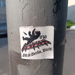 A sticker featuring a cartoon bear sprawled on a cot, with the text 'Dit is Berlin, Bitch!' and the area code 030. The style is bold and slightly edgy.