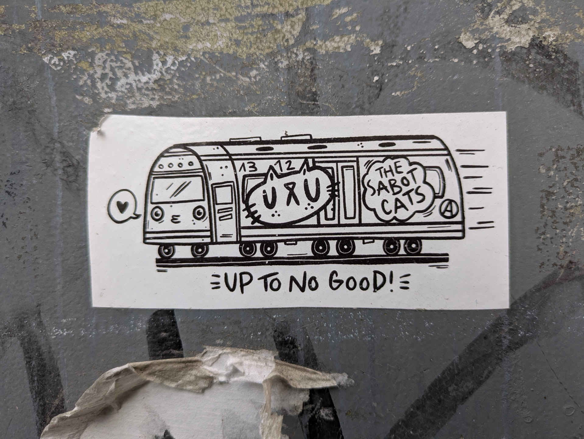 This black and white sticker shows a cartoon train speeding along tracks. Inside, cats can be seen looking out the windows, with one cat sporting a speech bubble containing "UXU". The train is labeled "The Sabot Cats" and below the train, the phrase "UP TO NO GOOD!" is printed.