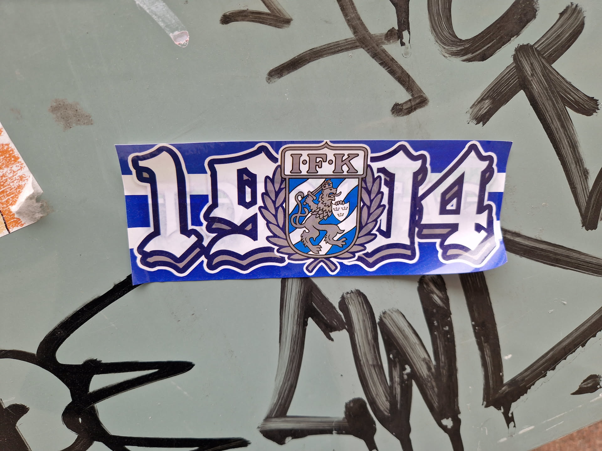 A blue and white sticker commemorating the year 1914 and featuring the logo of IFK, possibly a sports club or organization.  The logo includes a lion emblem.