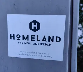 A sticker for Homeland Brewery in Amsterdam.  The sticker is white with black text and logo. It includes a website and Facebook page.