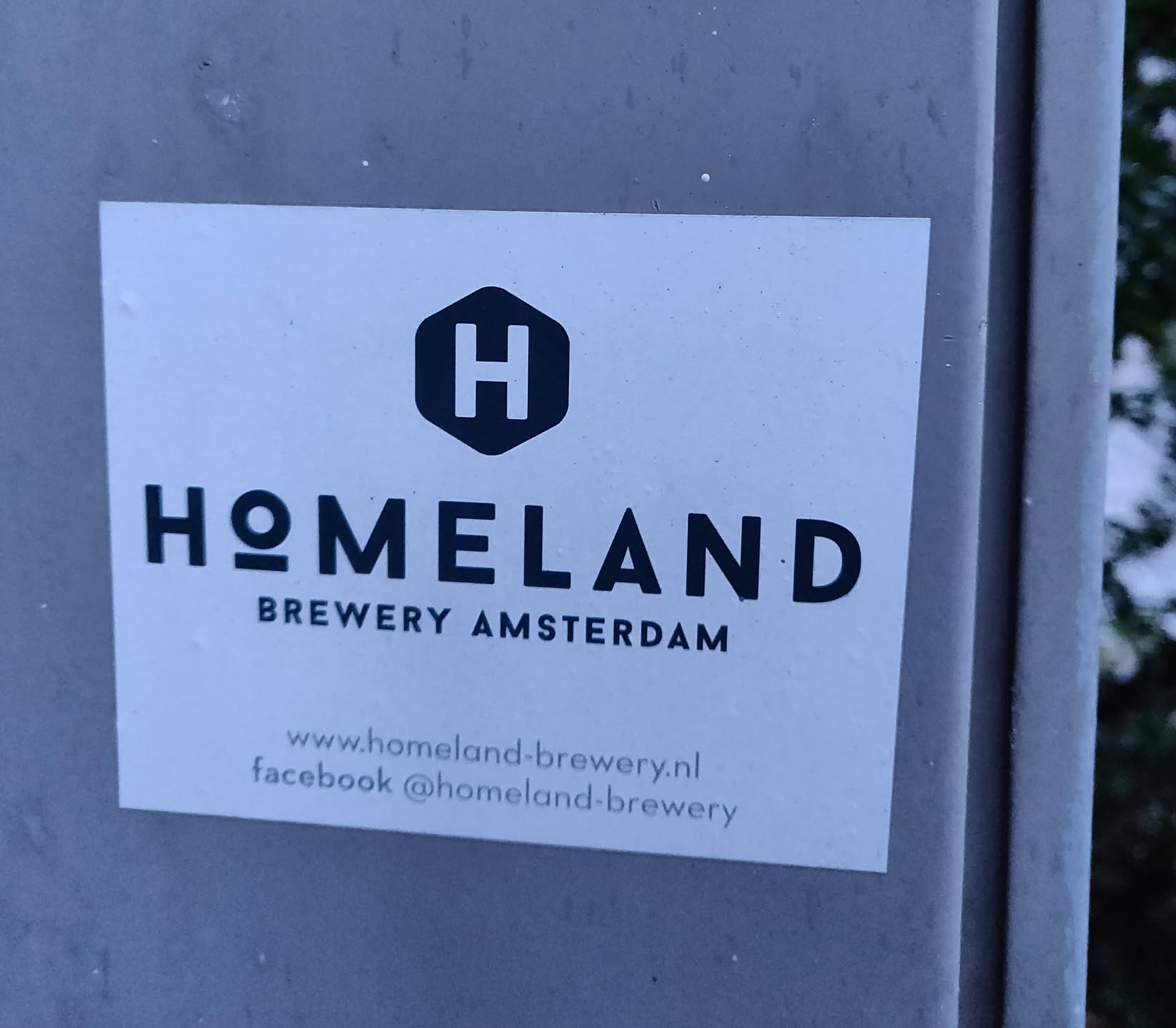 A sticker for Homeland Brewery in Amsterdam.  The sticker is white with black text and logo. It includes a website and Facebook page.