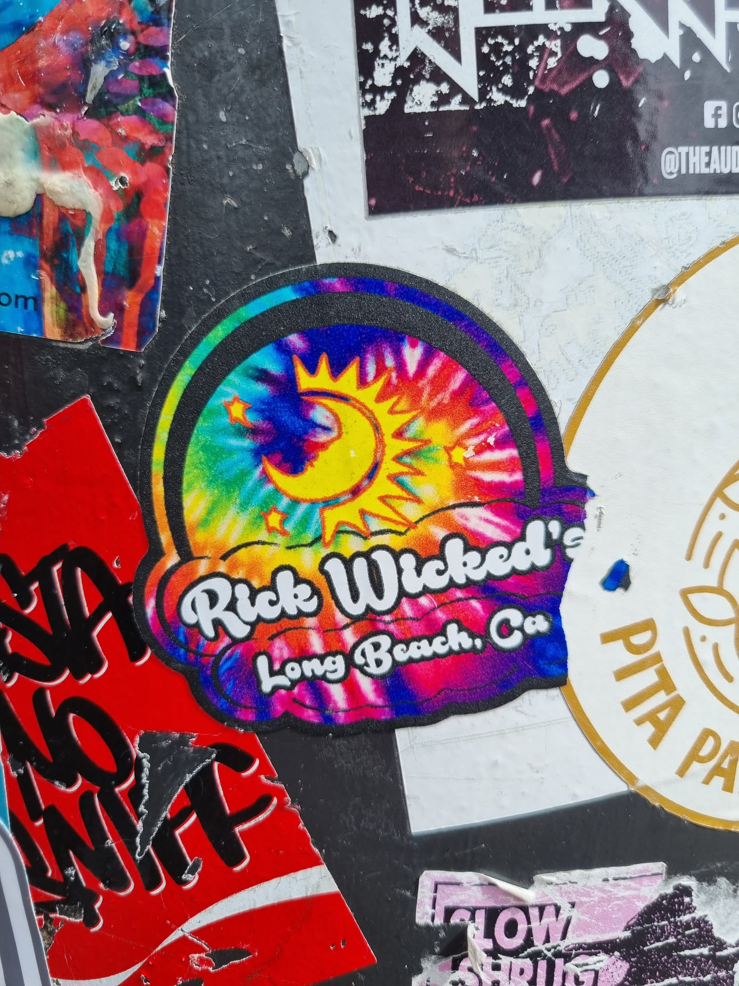 A tie-dye sticker with a sun and moon design. The text "Rick Wicked's Long Beach, Ca" is written on the sticker.