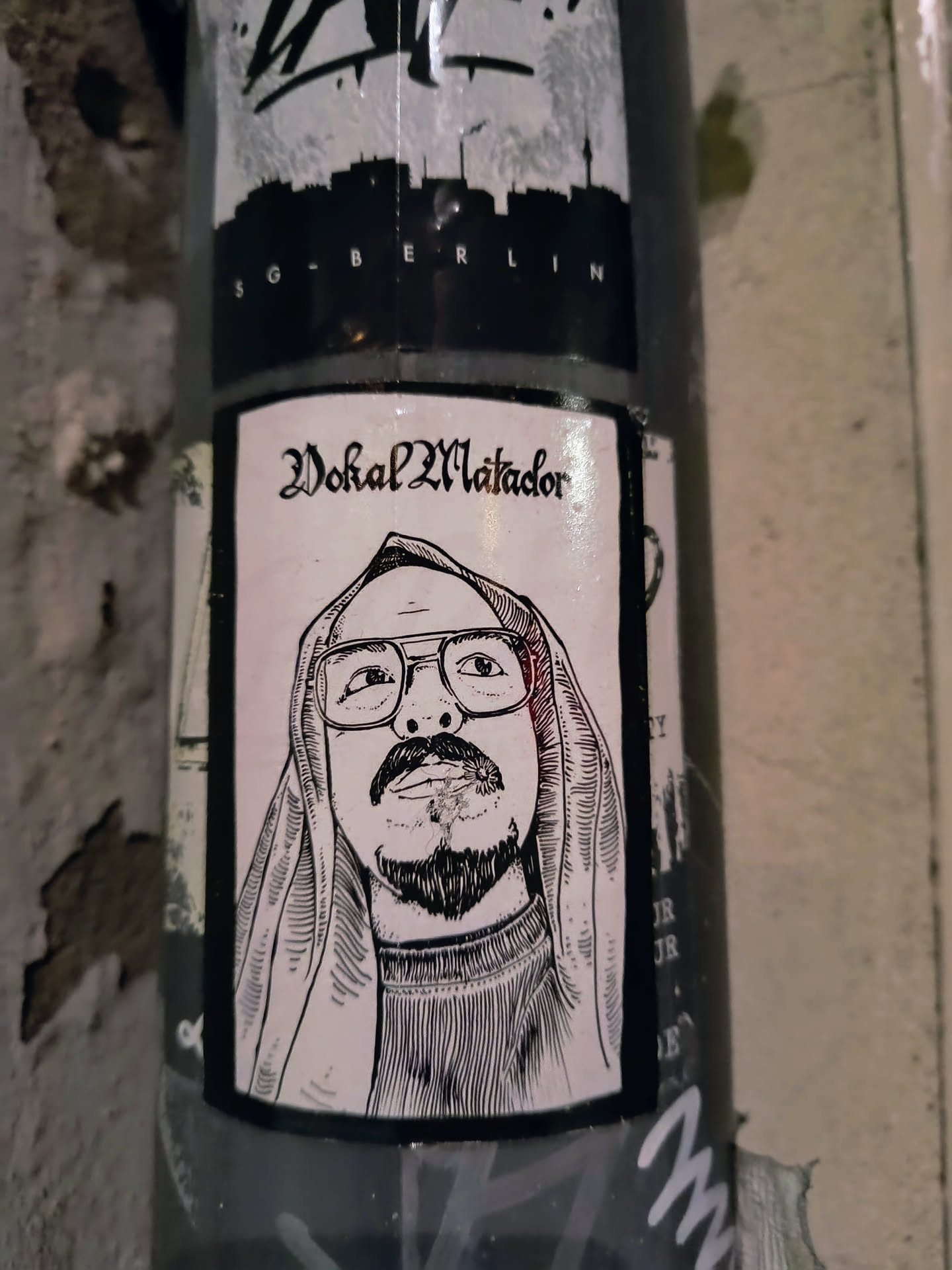 The sticker shows a black and white illustration of Vokal Matador, a person with glasses and a head covering, smoking a cigarette. The text 'Vokal Matador' is written in gothic font above the portrait.
