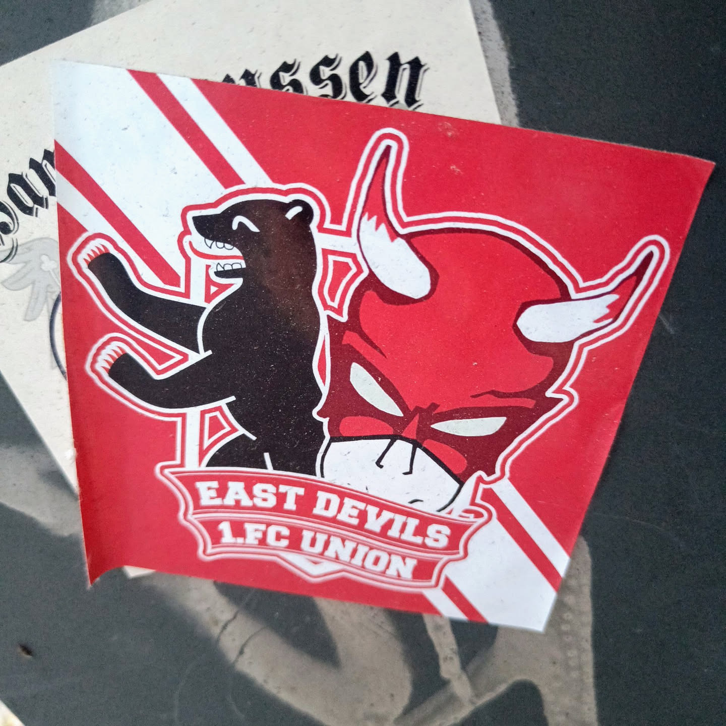 A red and black sticker featuring a bear and a devil's head, with the text "East Devils 1.FC Union" on a banner. The sticker likely represents a fan club or supporter group for the German football club 1. FC Union Berlin.