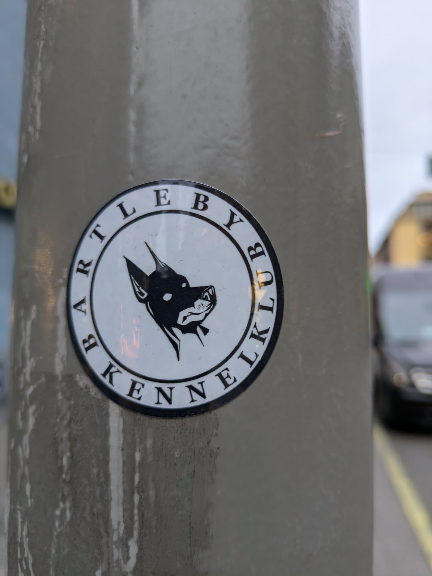 Round sticker with a black and white illustration of a dog's head in profile. The text 'Bartleby Kennel Club' circles the image.