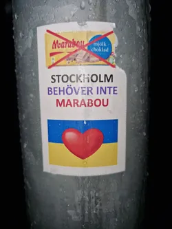 A sticker expressing support for Ukraine and boycotting the chocolate brand Marabou. It features a red heart on a Ukrainian flag and a crossed-out Marabou chocolate bar.