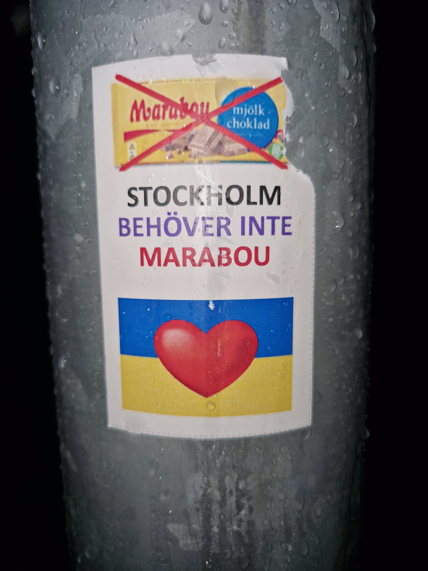 A sticker expressing support for Ukraine and boycotting the chocolate brand Marabou. It features a red heart on a Ukrainian flag and a crossed-out Marabou chocolate bar.