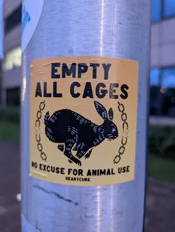 A sticker featuring a black rabbit running with chains on a yellow background. The text on the sticker says "EMPTY ALL CAGES" at the top and "NO EXCUSE FOR ANIMAL USE" with the logo Heartcure at the bottom.