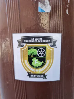 A sticker commemorating 10 years of Thüringer FC Erfurt, established in 2013.  The design features a crest with a tree, wheel, and a footballer.