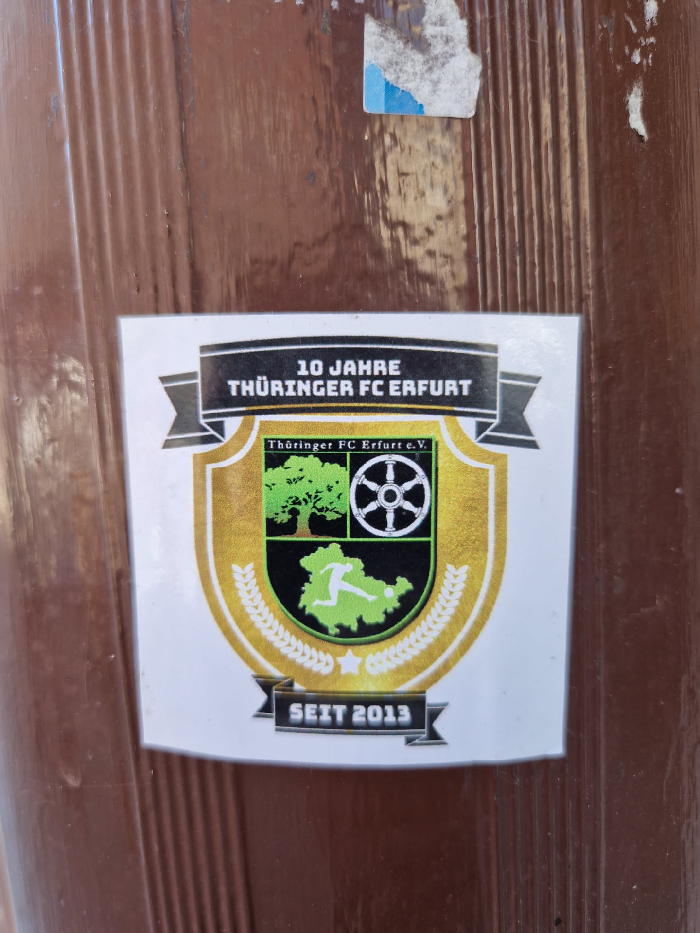 A sticker commemorating 10 years of Thüringer FC Erfurt, established in 2013.  The design features a crest with a tree, wheel, and a footballer.