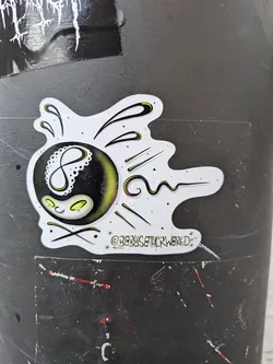 An irregularly shaped sticker with a white outline, featuring a stylized black 8-ball as its central element. The '8' on the ball is white and has a delicate, dotted, lace-like pattern on its left side. Below the '8', a small, anthropomorphic face is depicted with two glowing yellow-green oval eyes and a subtle, curved smile. The bottom portion of the 8-ball also emits a soft yellow-green glow. Emanating from the 8-ball are various black lines and dots, some accented with yellow-green, suggesting motion or energy against the white background. Small black speckles are scattered across the white areas of the sticker. Below the main design, the text '@BOBYSOTHERWORLD' is written in a stylized font, flanked by small starbursts.