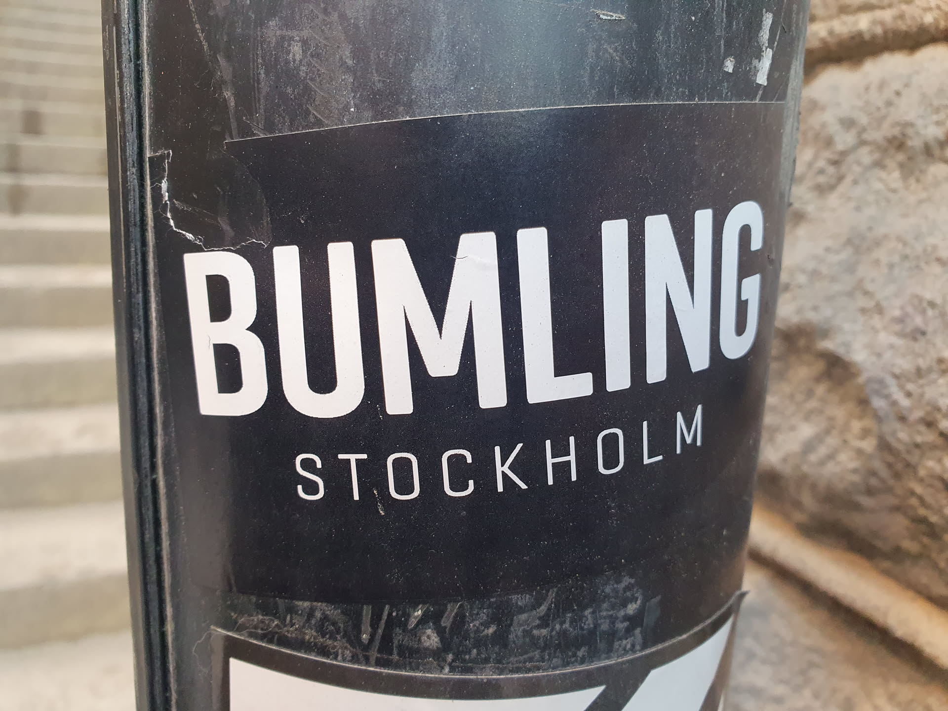 A black and white sticker with the text "BUMLING STOCKHOLM" on it. The sticker is slightly damaged.