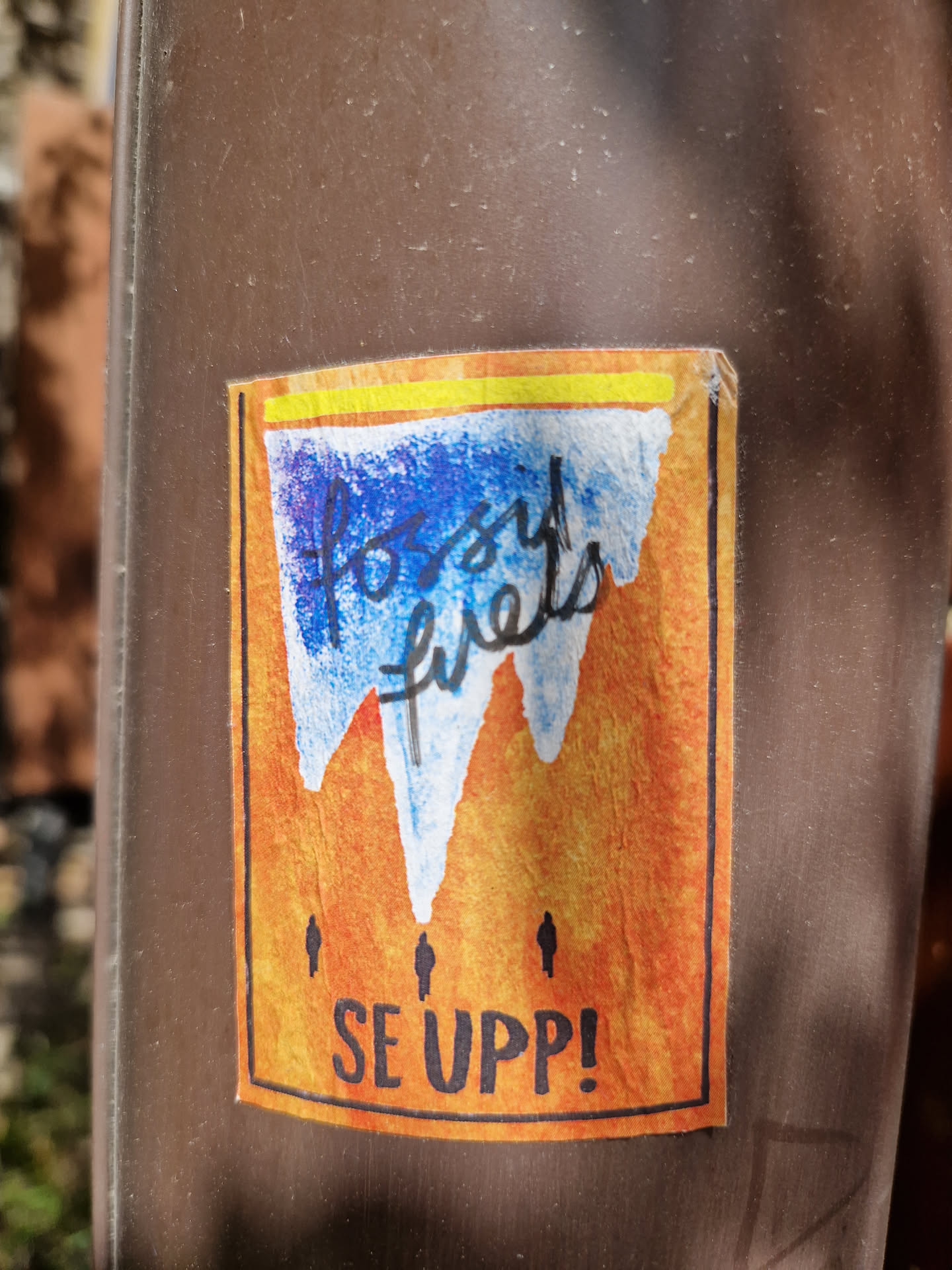 A sticker with a watercolor-like design depicting melting mountains representing fossil fuels. The text "Fossil fuels" is written in a stylized font, and the phrase "SE UPP!" (Swedish for "Wake up!") is written below.  The sticker features a yellow line across the top and small figures at the base of the mountains.