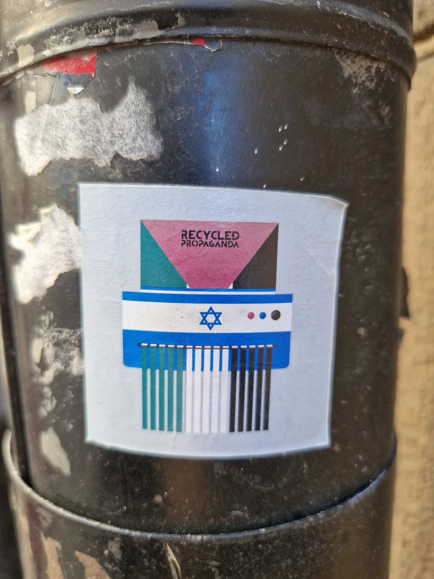 Sticker depicting a paper shredder with the Israeli flag being shredded into smaller pieces representing different colors and potentially ideologies. The sticker includes the text "Recycled Propaganda" at the top.