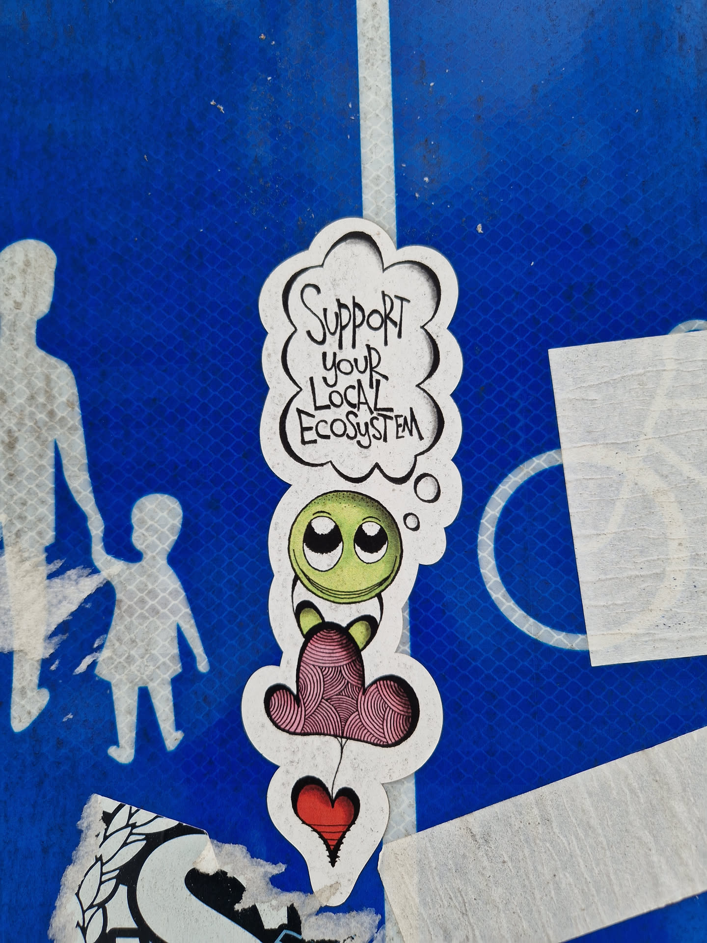 A cute sticker featuring a cartoon character with big eyes sitting on a pink cloud-like shape, with a red heart below. The sticker has the text 'Support Your Local Ecosystem' written in a thought bubble above the character.