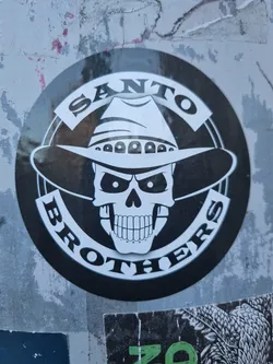 Black and white sticker of a skull wearing a cowboy hat. The words \"SANTO BROTHERS\" are written around the skull.