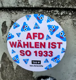 A round sticker with a white background and blue poop emojis.  The text "AfD Wählen ist so 1933" is written in red.  The bottom of the sticker has the logo and website for taz.