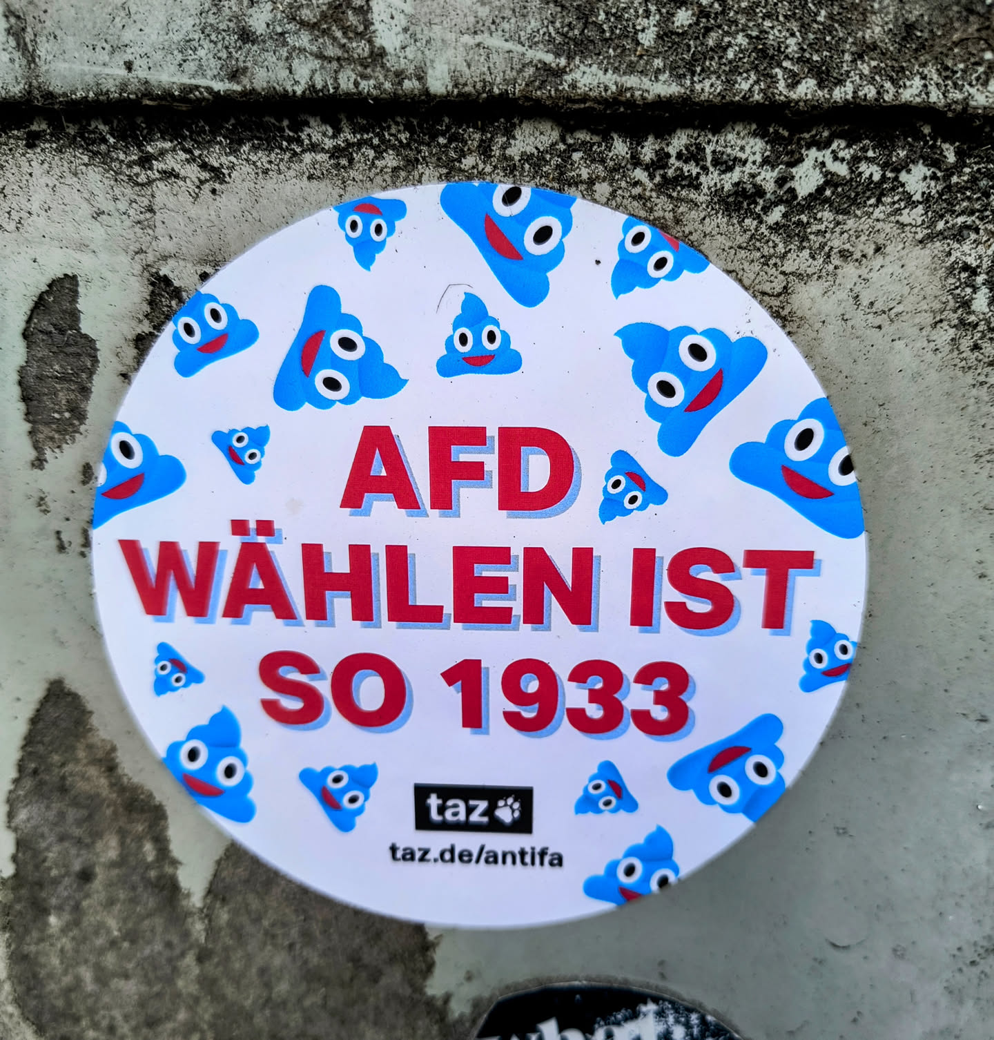 A round sticker with a white background and blue poop emojis.  The text "AfD Wählen ist so 1933" is written in red.  The bottom of the sticker has the logo and website for taz.