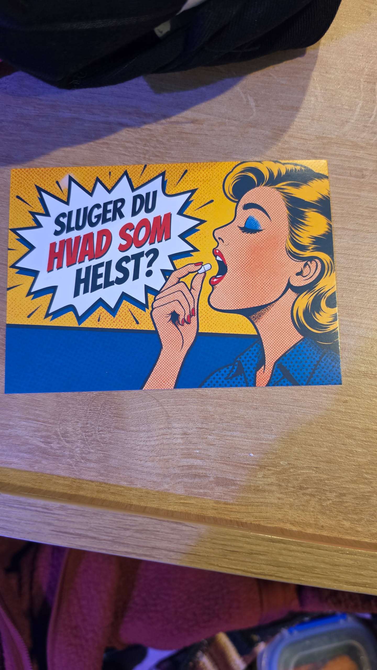 A rectangular sticker designed in a classic vintage comic pop-art style with Ben-Day dot shading. On the right side, a blonde woman in profile with bright blue eye shadow and red lipstick raises a white pill to her open mouth. To the left, a jagged white speech bubble framed in dark blue pops out against a yellow background, containing the bold text 'SLUGER DU HVAD SOM HELST?' with the top and bottom words in dark blue and the middle words in red.