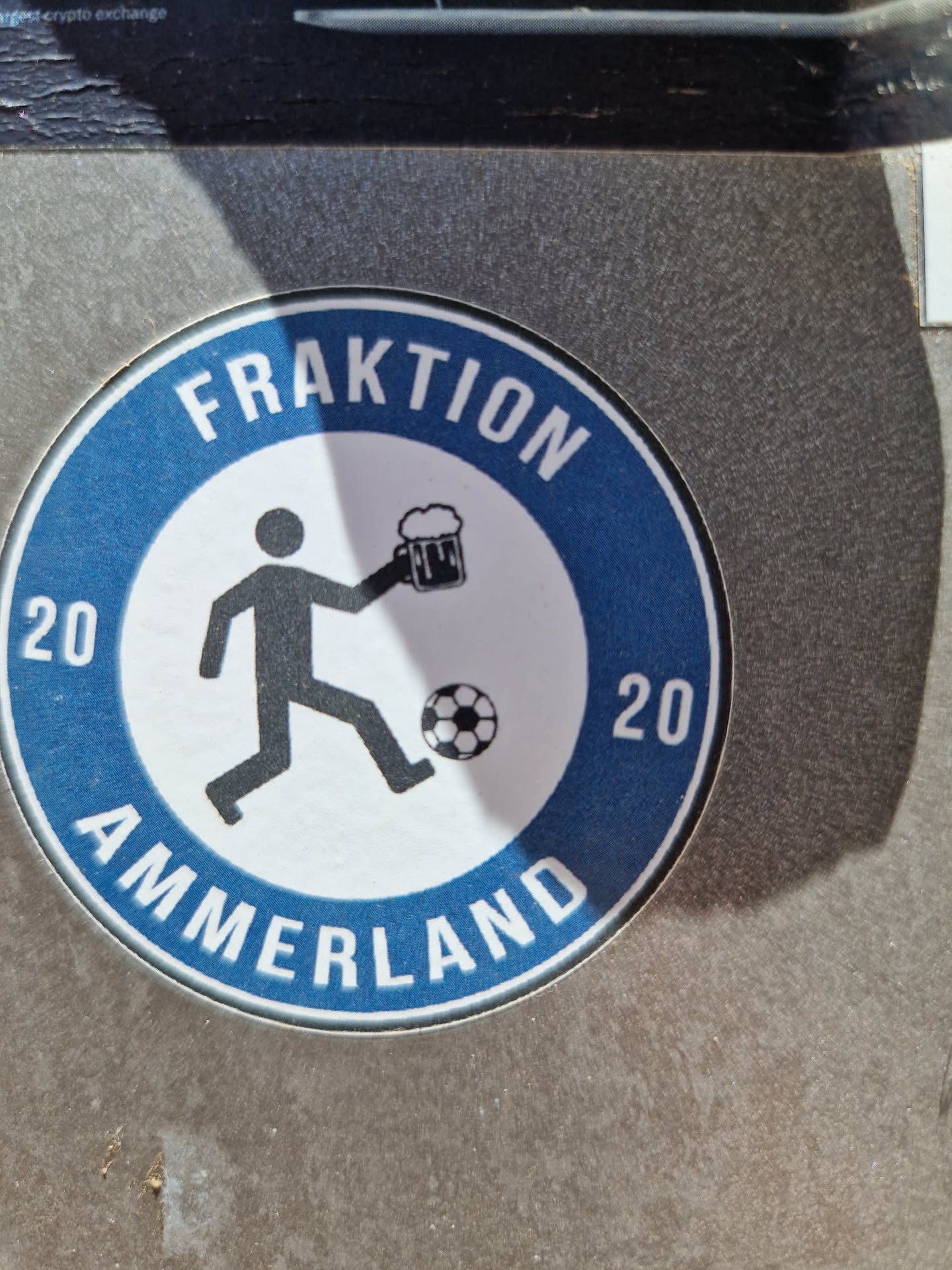 Round blue and white sticker with a pictogram of a person kicking a football and holding a beer mug. The text Fraktion Ammerland 2020 is written around the circle.