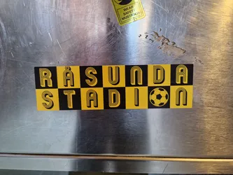 A yellow and black sticker with the words Räsunda Stadion and a soccer ball in the center. The text is in a retro style font.