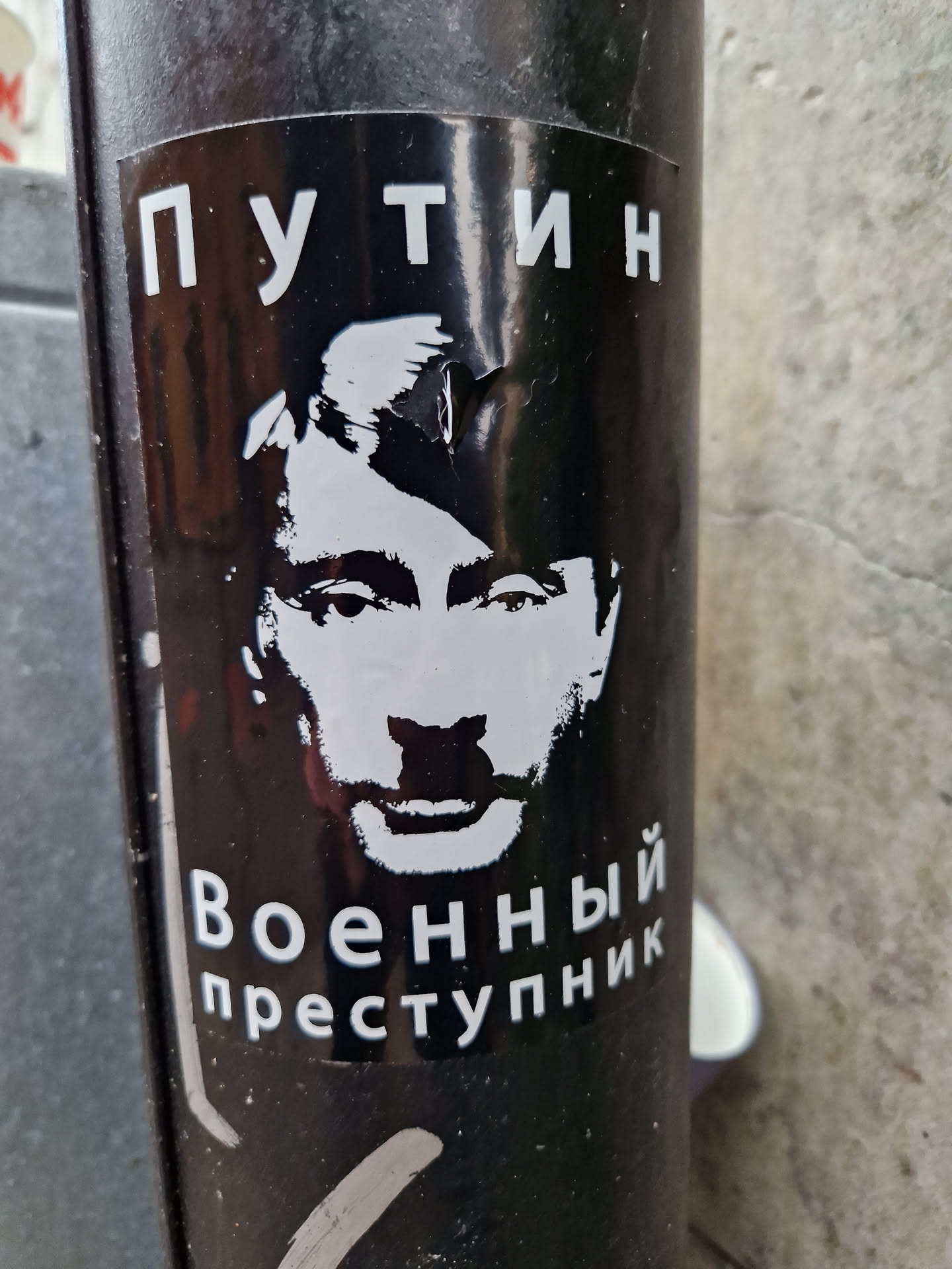 Black and white sticker featuring a stylized portrait of Vladimir Putin with the text "Putin" at the top and "War Criminal" at the bottom in Russian (Путин Военный преступник).