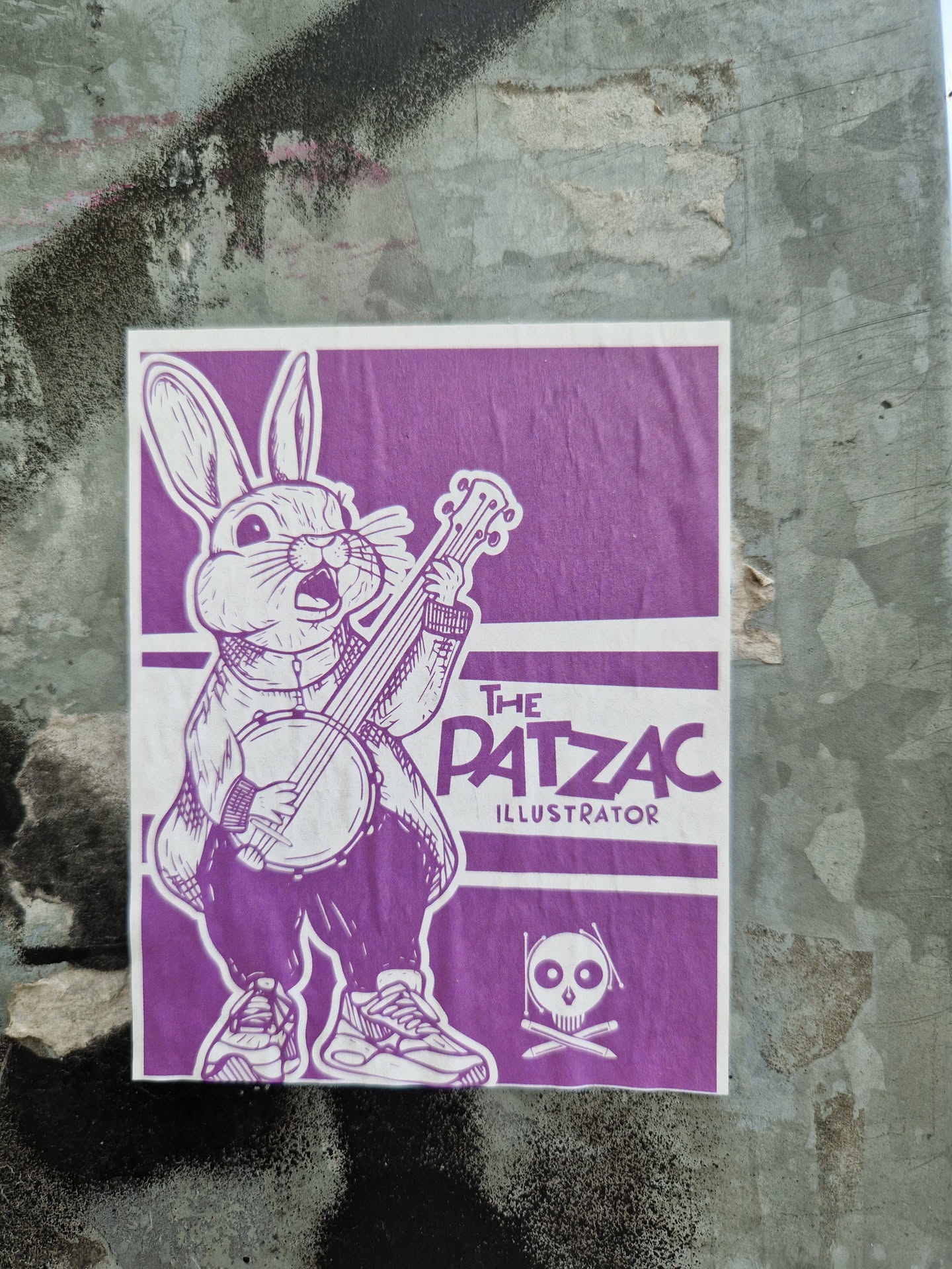 Purple sticker featuring a rabbit playing a banjo. The artist's name, "The Patzac Illustrator," is printed at the top. A skull and crossbones symbol is also present.