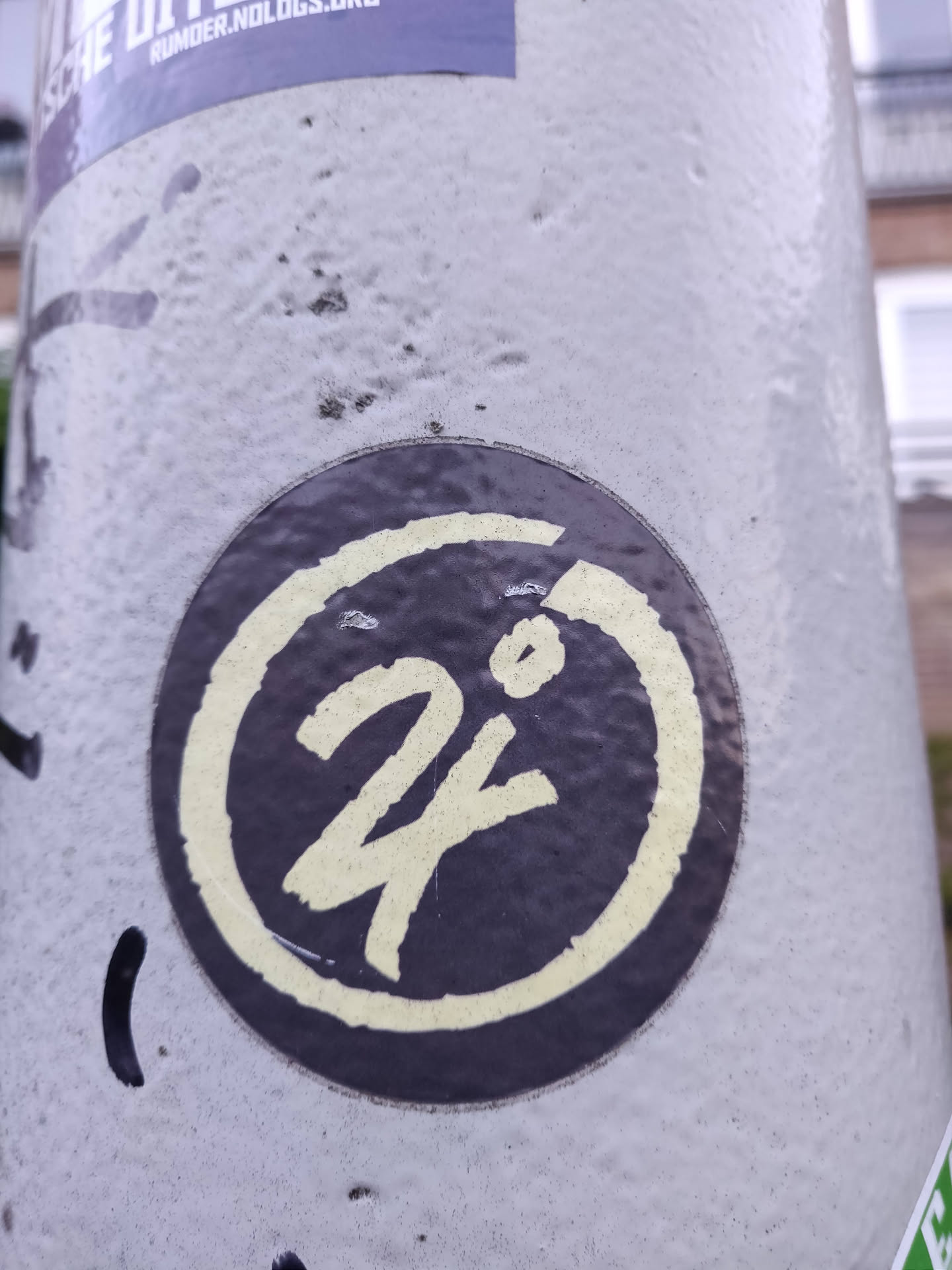 A round sticker featuring a dark-colored background with a lighter yellow-cream colored stylized '24' in the center. The '24' has a slightly hand-drawn look.  The number is encircled by a thicker ring of the same lighter color.
