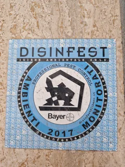 A blue and white sticker with the text DISINFEST and IGIENE AMBIENTALE S.R.L.S., indicating pest control services.  The central logo features a house and the Bayer logo. The year 2017 is also visible. The sticker's border is patterned with repeating house icons.  An email address is included: disinfest@libero.it
