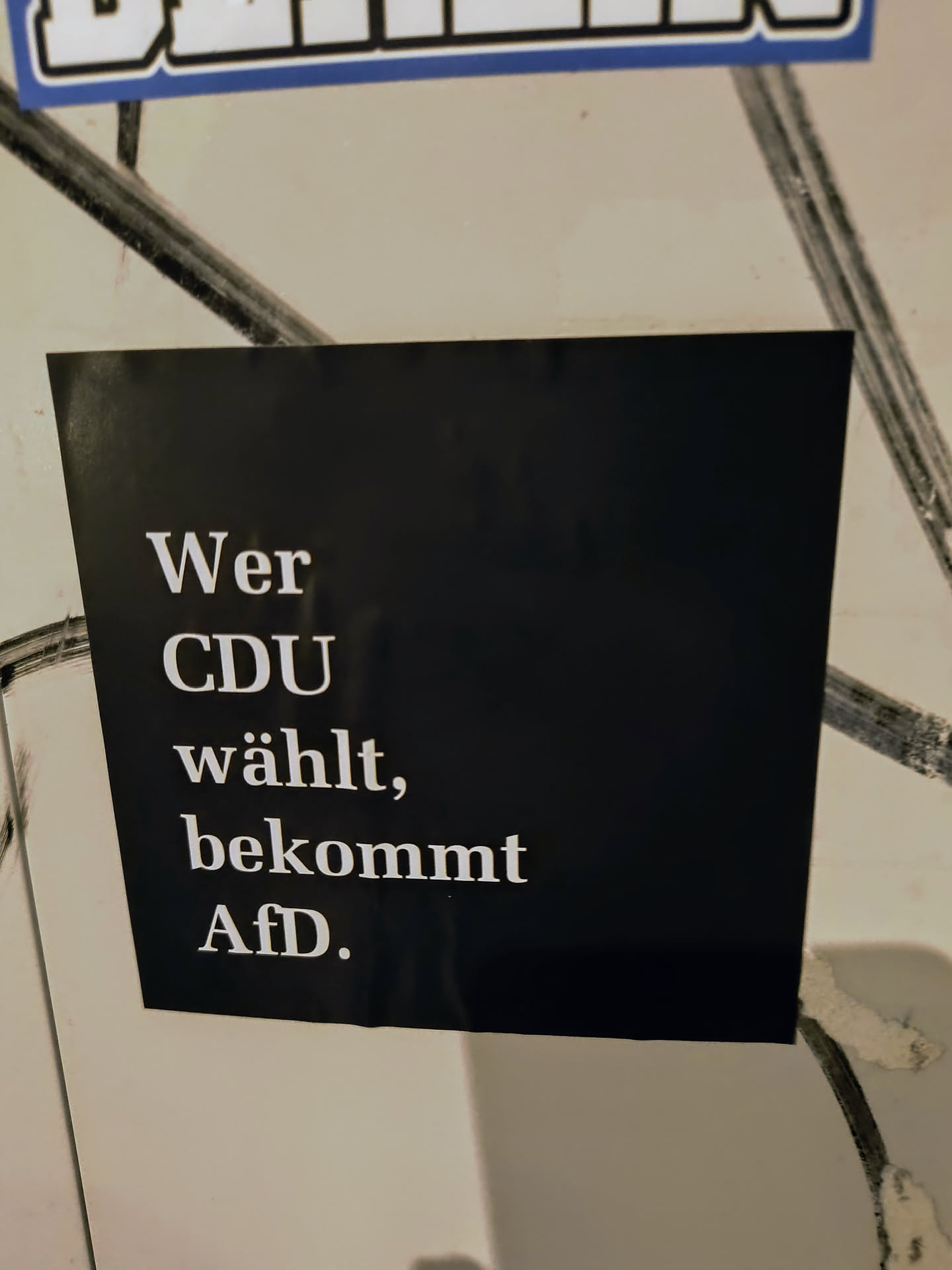 A political sticker with a black background and white text that says "Wer CDU wählt, bekommt AfD." It translates to "Whoever votes for CDU, gets AfD."