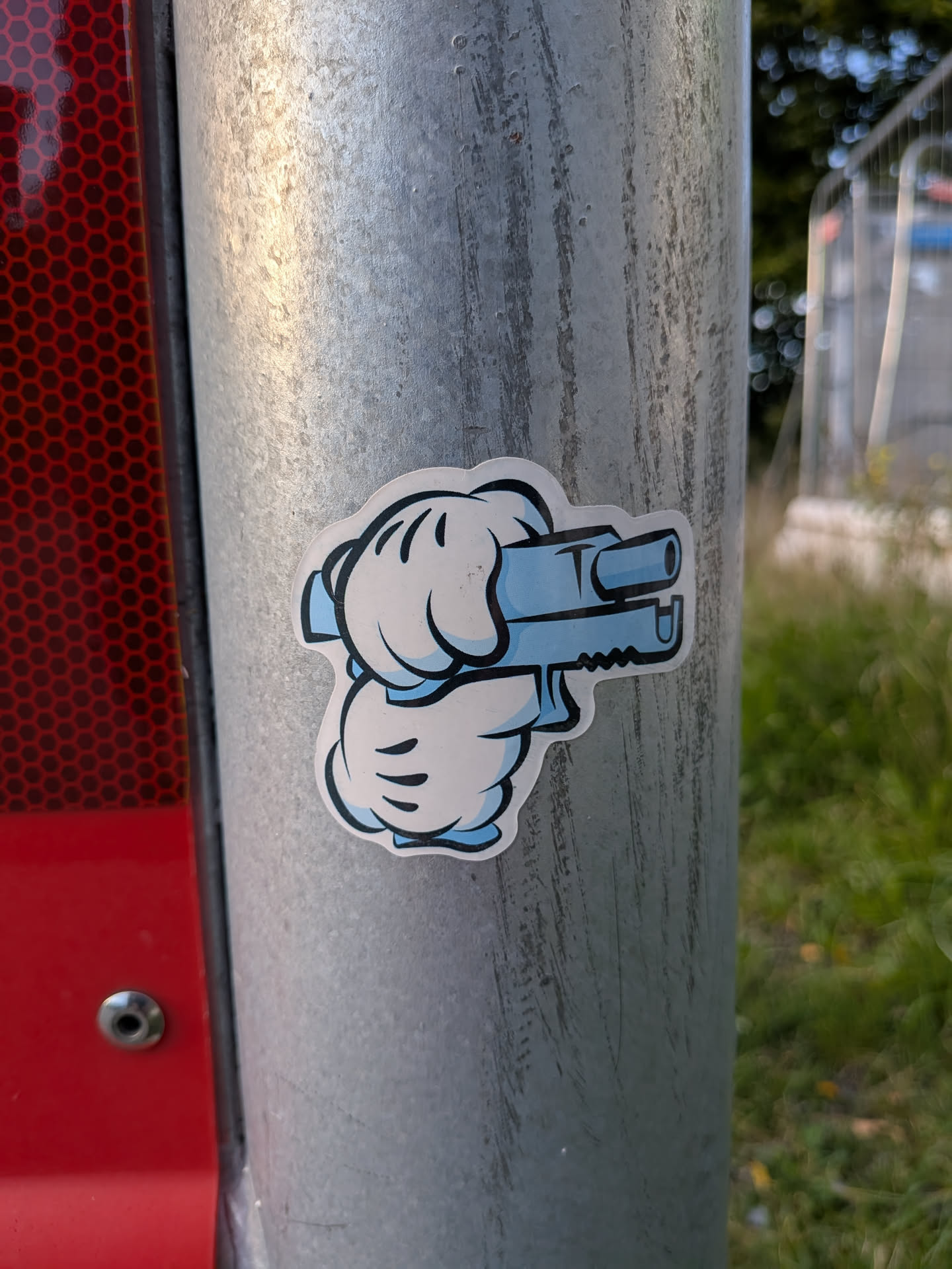 The sticker features two stylized white gloves, reminiscent of Mickey Mouse's hands, holding a light blue, blocky toy gun. The gloves are outlined in black, and the gun has black accents and a serrated edge. The background of the sticker is white with a subtle blue shading around the edges, and it has a distinct die-cut shape.