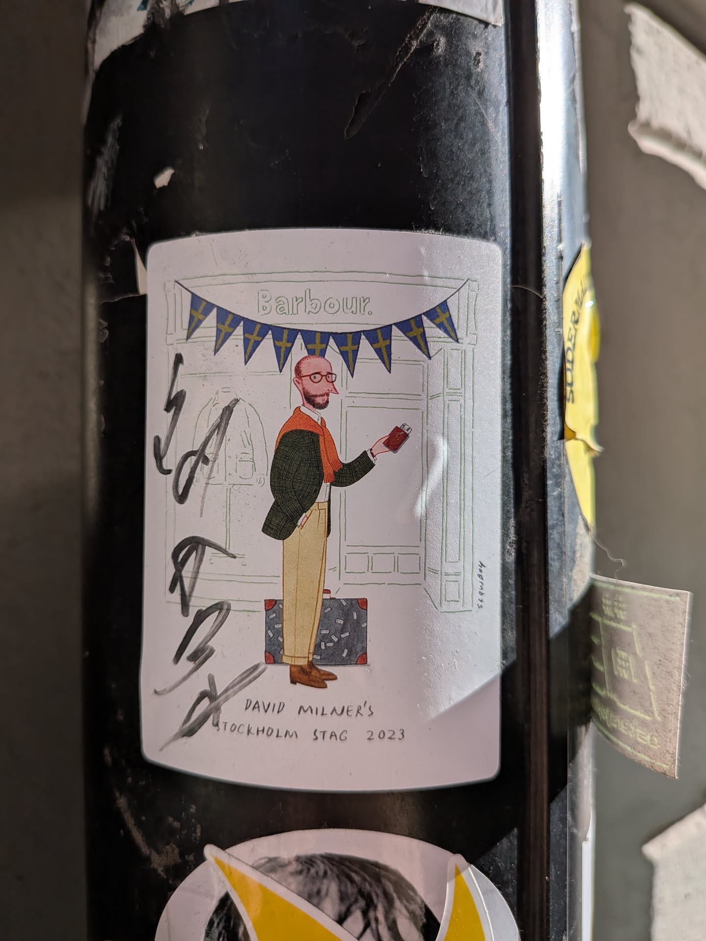A rectangular sticker with rounded corners, featuring a whimsical illustration on a white background. The central figure is a bespectacled man with a beard, dressed in a green Barbour-style jacket, an orange scarf, and tan trousers, holding a small red item. Behind him is a minimalist line drawing of a storefront, presumably a Barbour shop, adorned with a string of blue and yellow pennant flags, reminiscent of the Swedish flag. A small suitcase sits at his feet. The sticker includes the text 'Barbour.' at the top, 'slowboy' vertically on the right, and 'DAVID MILNER'S STOCKHOLM STAG 2023' at the bottom. There is also some illegible black marker writing on the left side of the sticker.