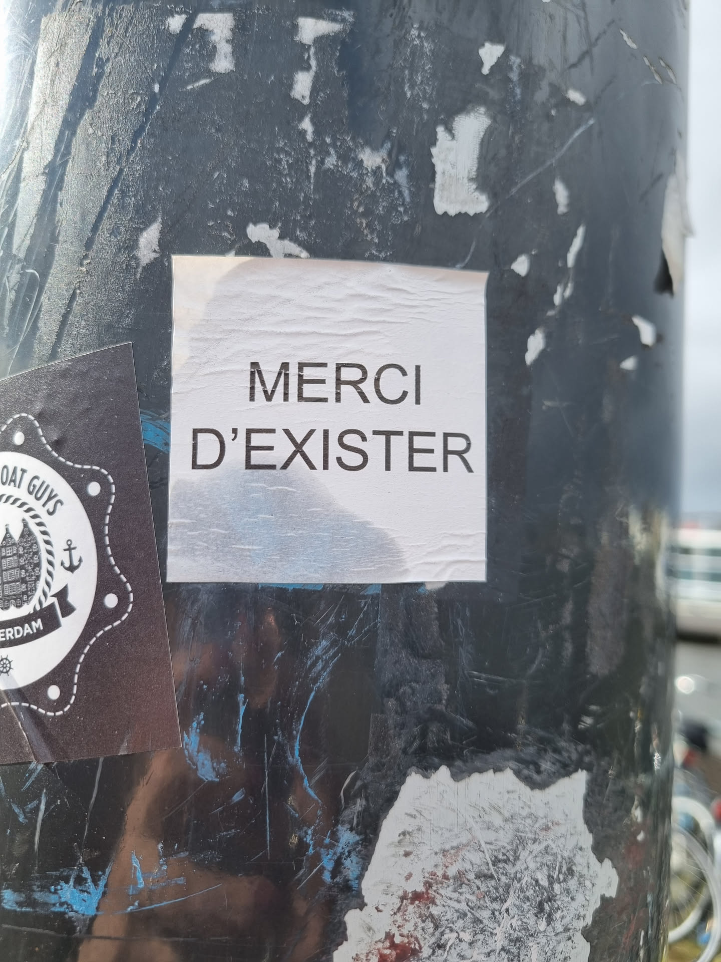 A simple, yet impactful message of gratitude.  The sticker features the French phrase "Merci d'exister," which translates to "Thank you for existing." It is printed in a straightforward, sans-serif font on a white background.