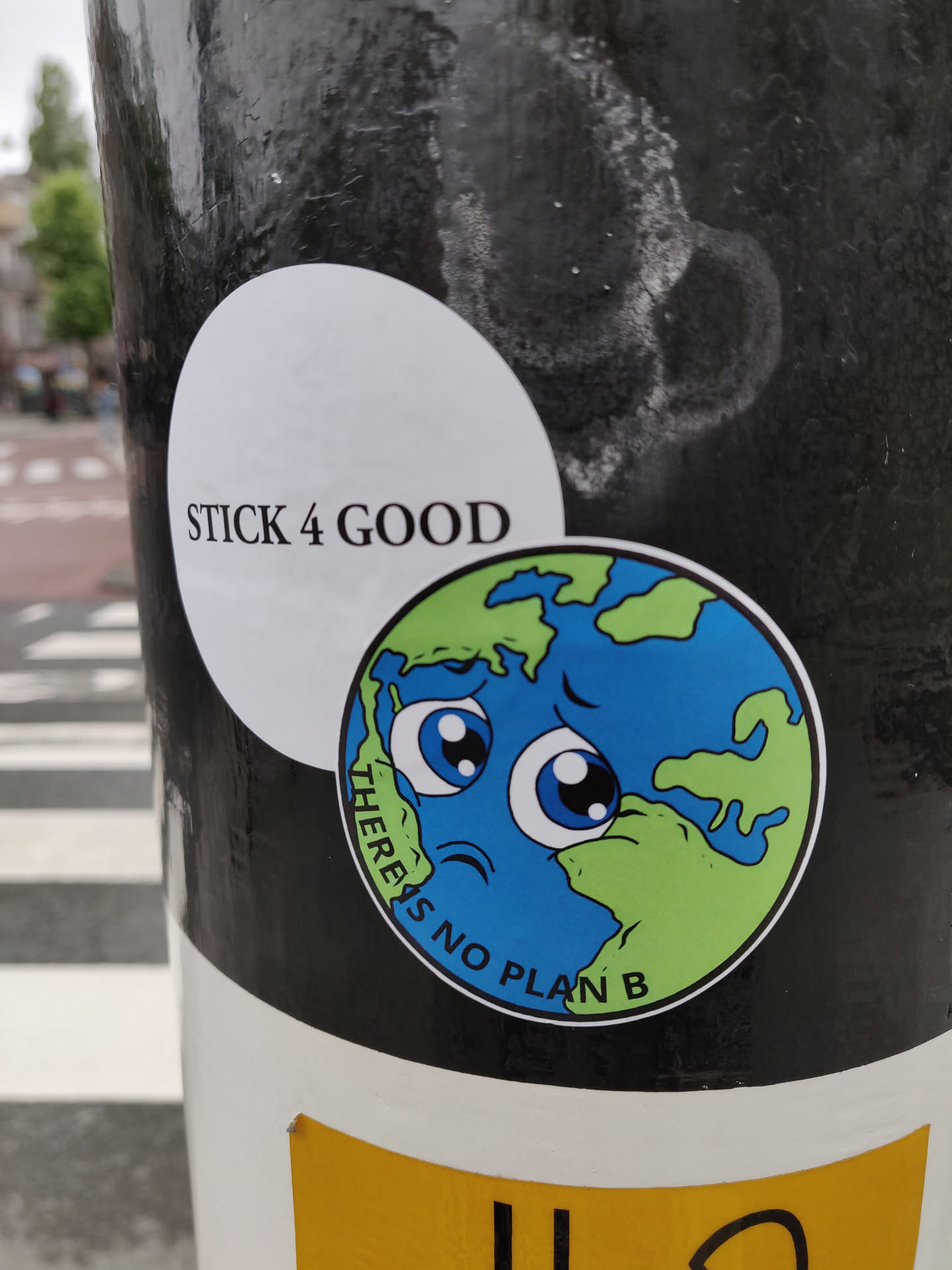 A round sticker with a cartoon illustration of the earth with a sad face. The text 'There is no plan B' is written around the illustration. Another sticker is on top of this one, with the text 'Stick 4 Good'.