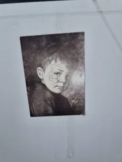 A monochrome sticker featuring a close-up portrait of a boy with a melancholic expression. The image is reminiscent of vintage photography or a painting.