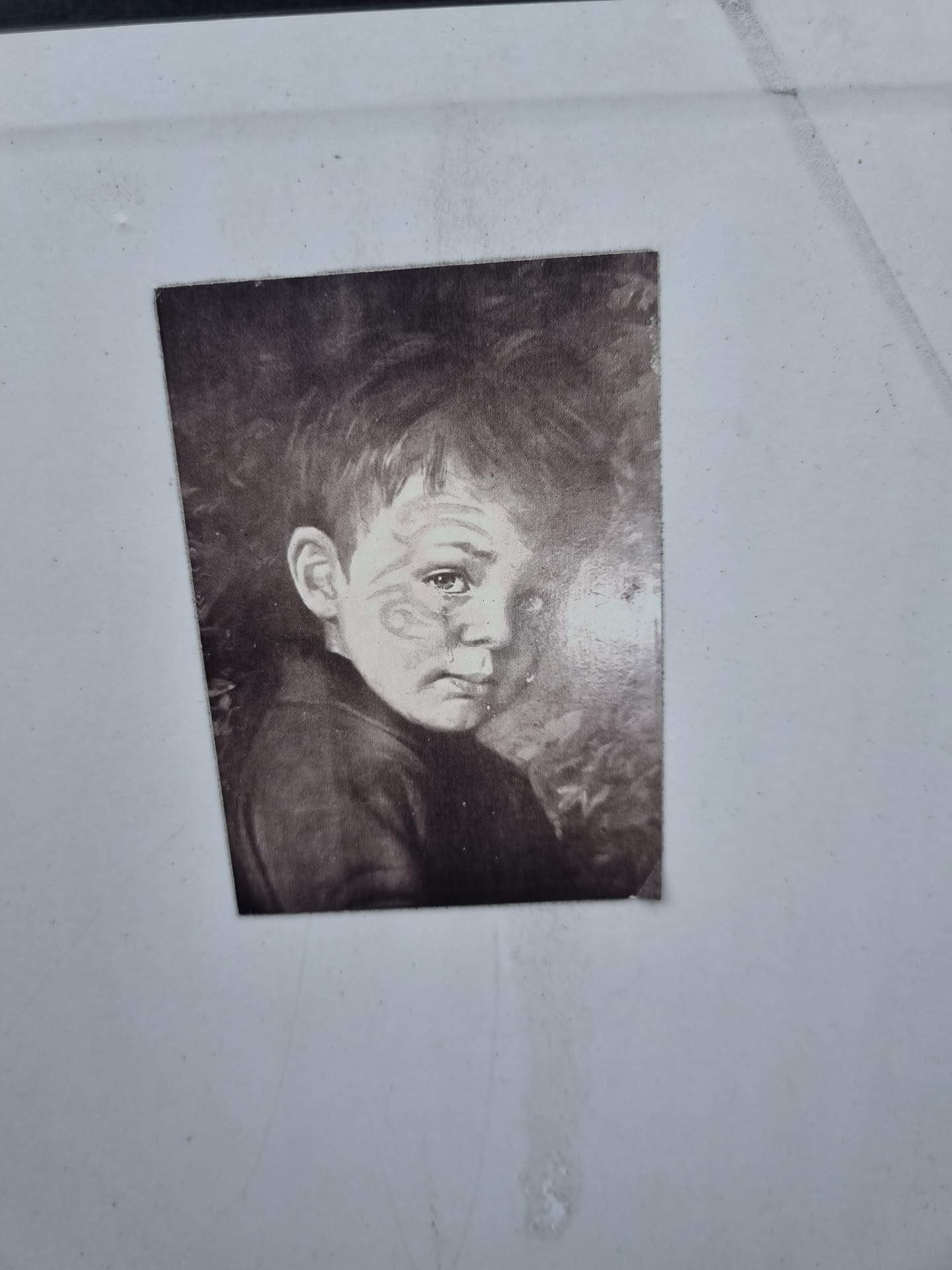 A monochrome sticker featuring a close-up portrait of a boy with a melancholic expression. The image is reminiscent of vintage photography or a painting.