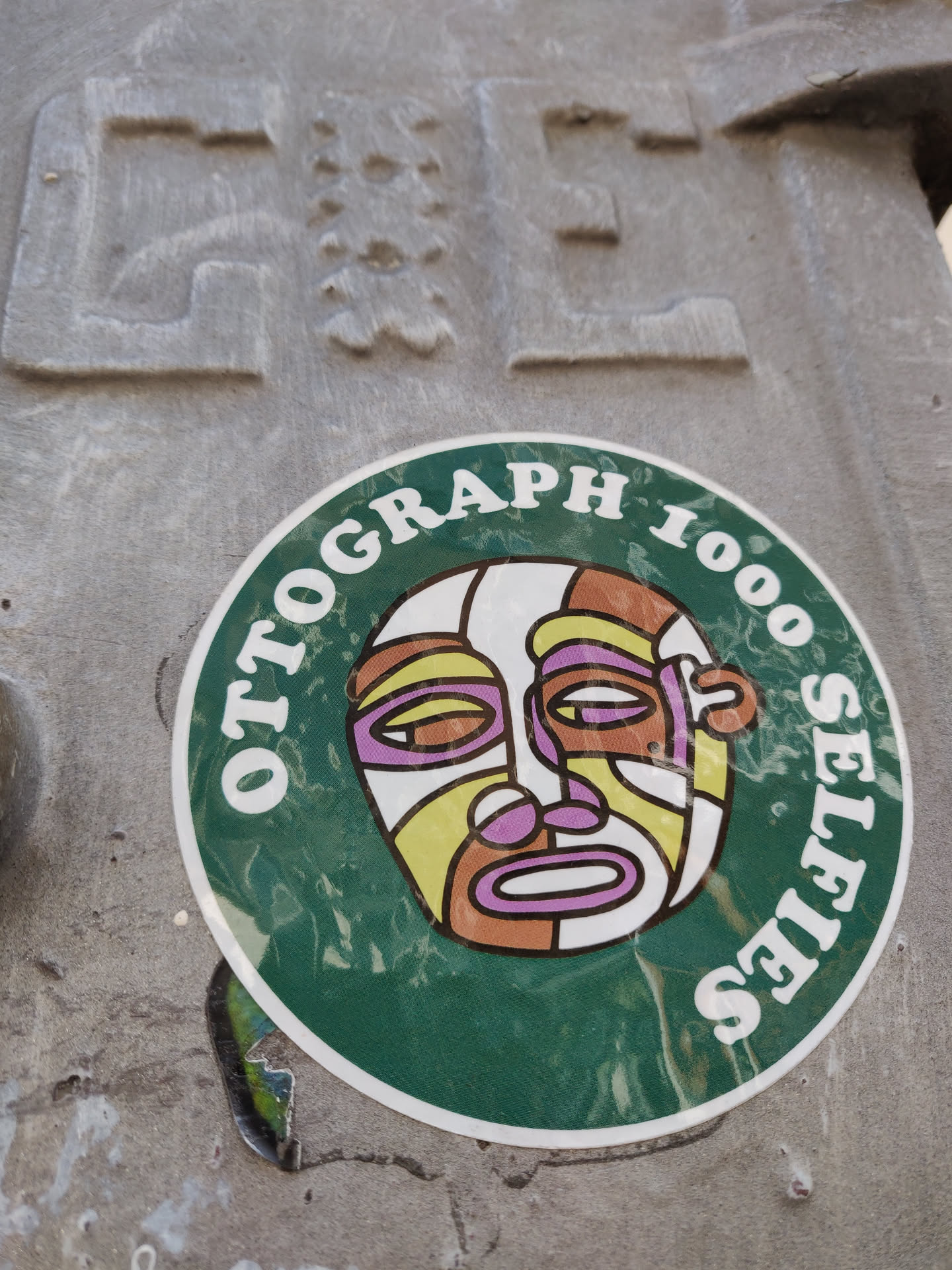 Round green sticker with illustration of a stylized face and the text "Ottograph 1000 Selfies".