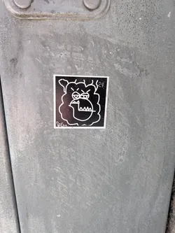A square sticker featuring a stylized, cartoonish character's head in white outline against a solid black background. The character has a thick, wavy outline suggesting fur or hair, prominent furrowed eyebrows, small oval eyes, and a large, open mouth revealing sharp, triangular teeth. Its expression conveys a sense of grumpiness or annoyance. In the bottom left corner, the signature 'Soem' is written in a stylized script, and in the top right corner, the numbers '24.' are visible.
