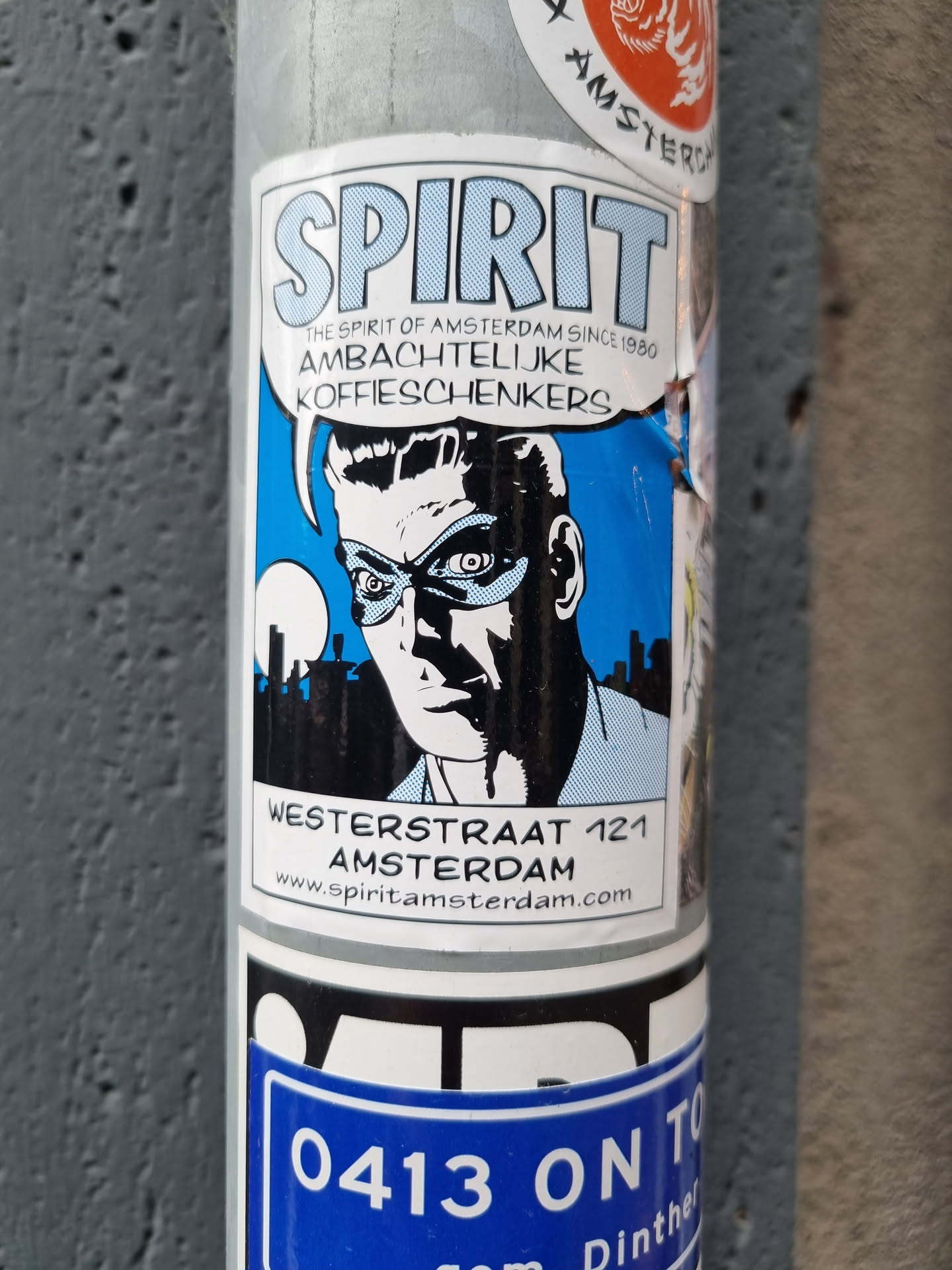 A sticker featuring a comic-style illustration of a man with a mask,  text indicating it represents the spirit of Amsterdam since 1980, and an address: Westerstraat 121 Amsterdam.  A website address is also included.