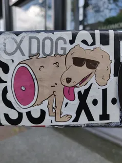 A sticker featuring a cartoon dog wearing sunglasses. The dog has a piece of meat on its behind. The sticker is on a pole outside.