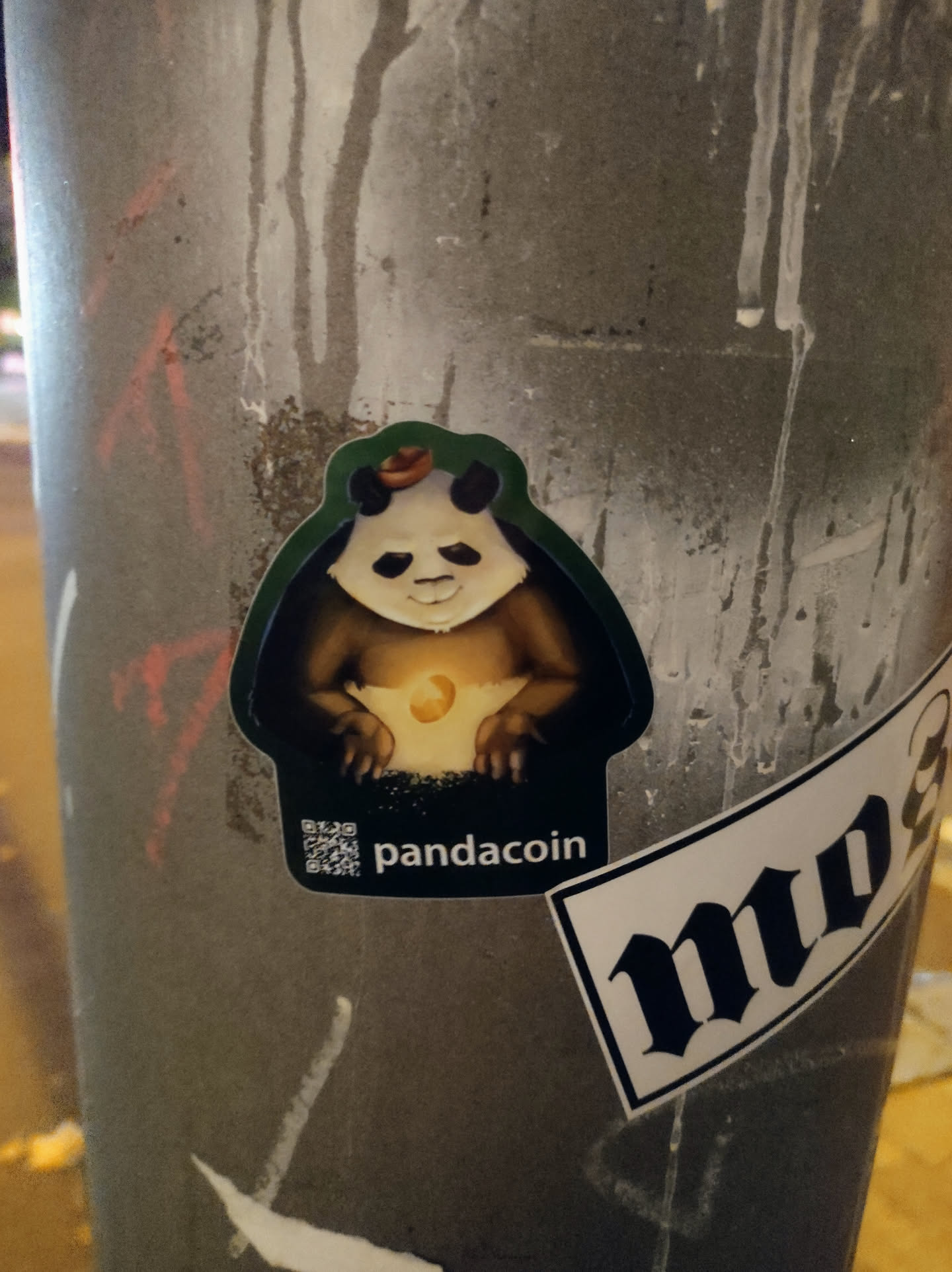 A sticker featuring a cartoon panda wearing a hat and holding a moon. The text 'pandacoin' is visible at the bottom of the sticker, along with a QR code. 