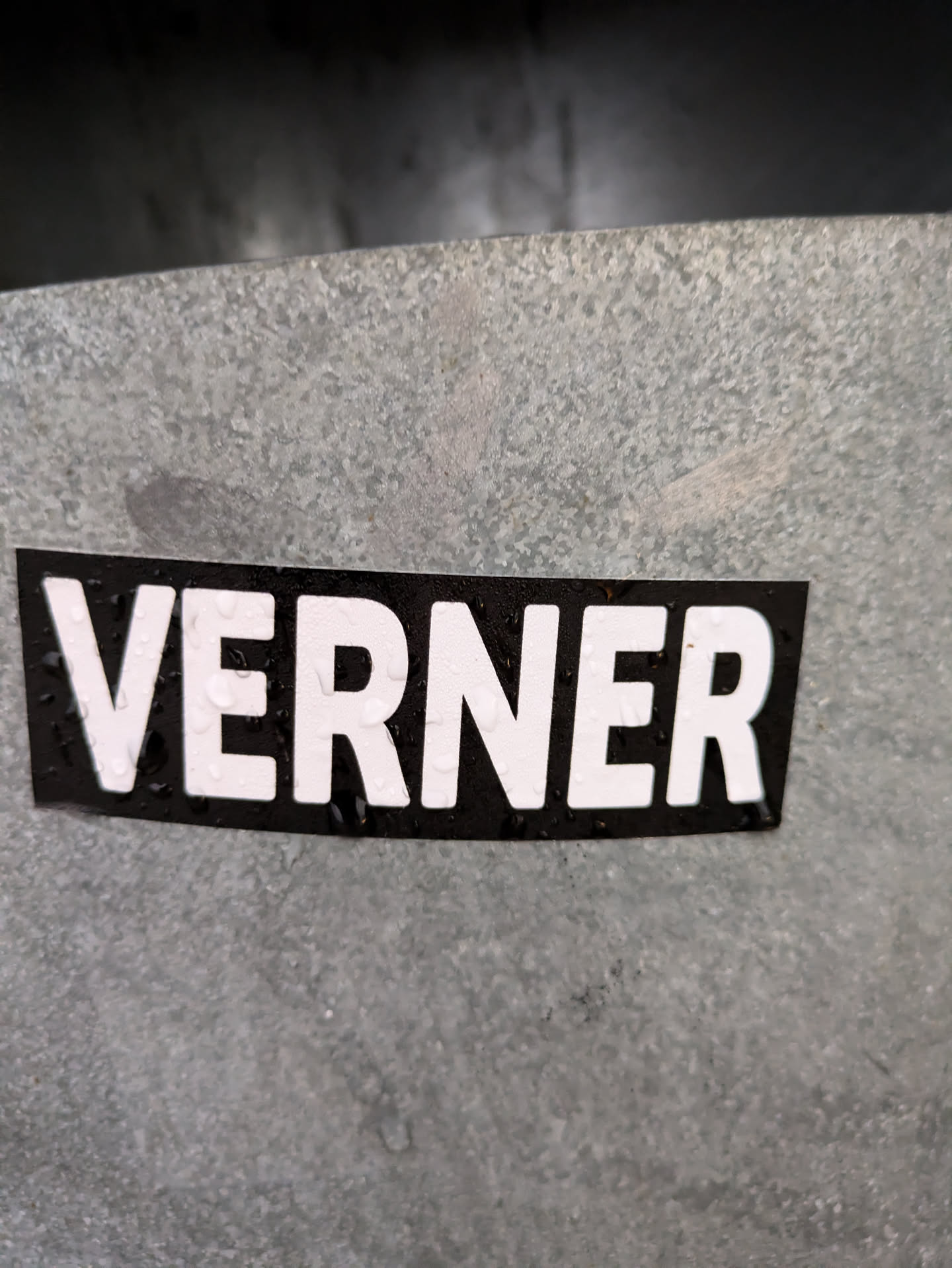A black and white sticker with the name VERNER written in capital letters. The sticker is affixed to a gray metallic surface.