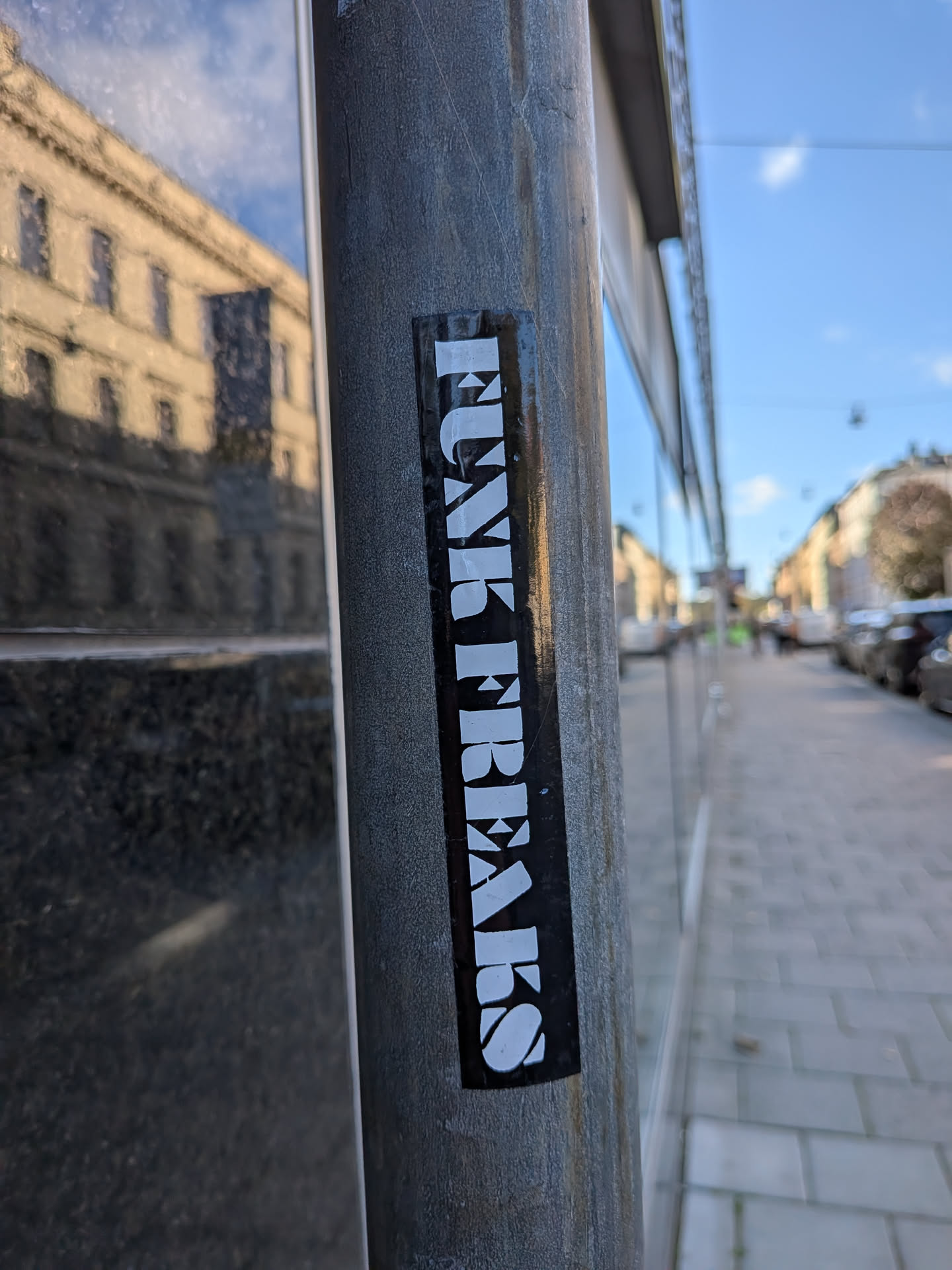 A vertical, rectangular sticker with a glossy black background adhered to a gray metal post along a sidewalk. The sticker features the text 'FUNK FREAKS' running vertically from top to bottom in bold, chunky, stylized white uppercase serif lettering.