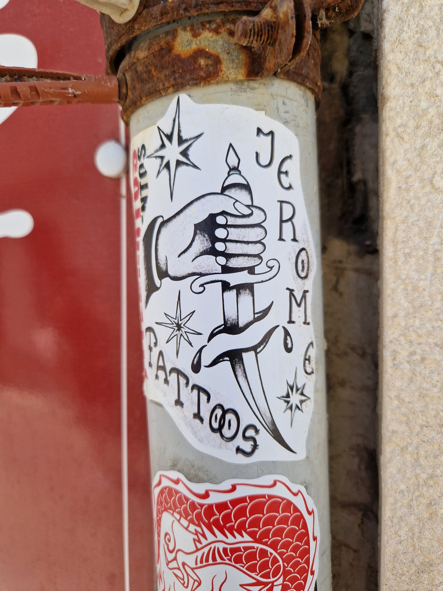 A sticker featuring a traditional tattoo flash design of a hand holding a dagger. The sticker includes the text "JEROME TATTOOS" and decorative elements like stars and blood drops. 