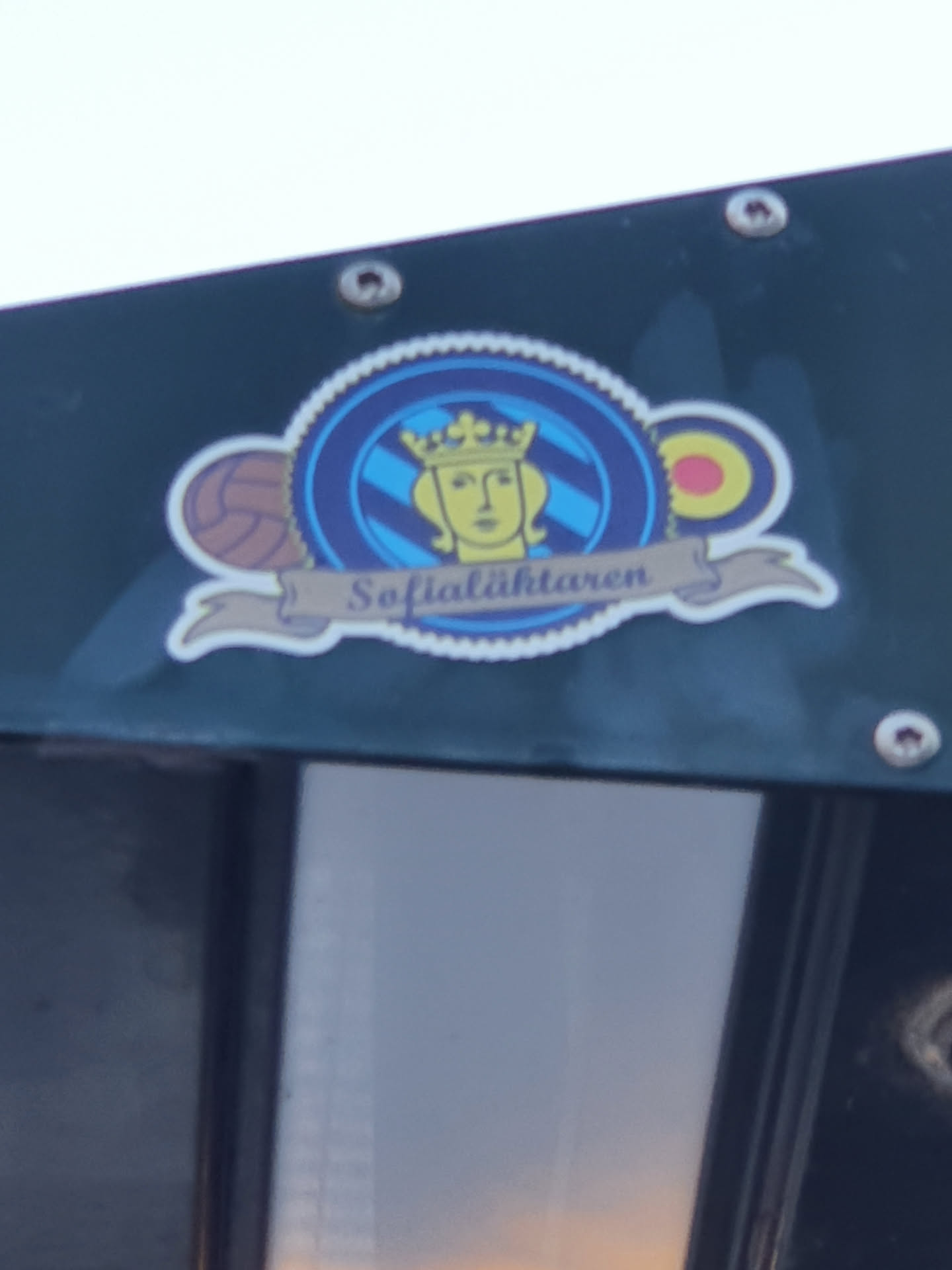 A sticker featuring a crest with a crowned woman's face, along with imagery of sports balls. The text 'Sofialightharen' is visible on a banner below the main emblem.