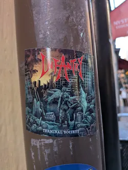 A rectangular sticker depicting a post-apocalyptic, ruined urban landscape. In the center, a soldier wearing combat gear and a helmet stands with his back turned, looking out over collapsed buildings and rubble. To his right, a tattered pale flag is planted in the debris. Above the skyline, the band name 'INFANTRY' is displayed prominently in sharp, spiky red metal lettering with a white outline. Along the bottom edge, the text 'TERMINAL SOCIETY' is printed in white capital letters.